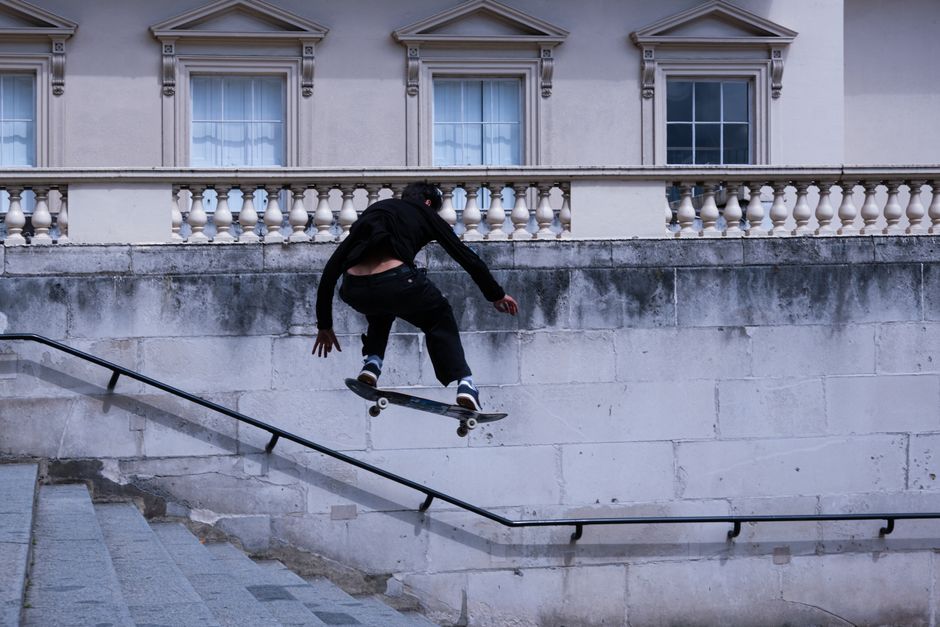 A skateboarder executing a mid-air trick on city stairs against a classic urban backdrop.