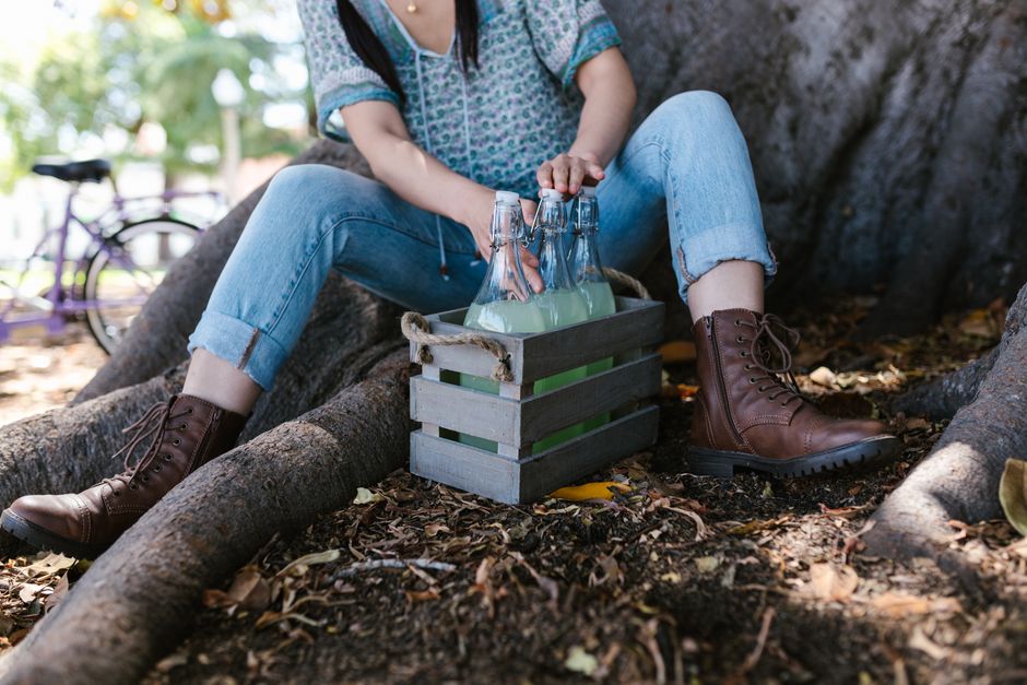 Bottles in a wooden crate beside a person sitting under a tree.