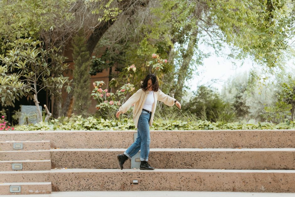 A cheerful woman walks down steps surrounded by lush green trees in a park setting.