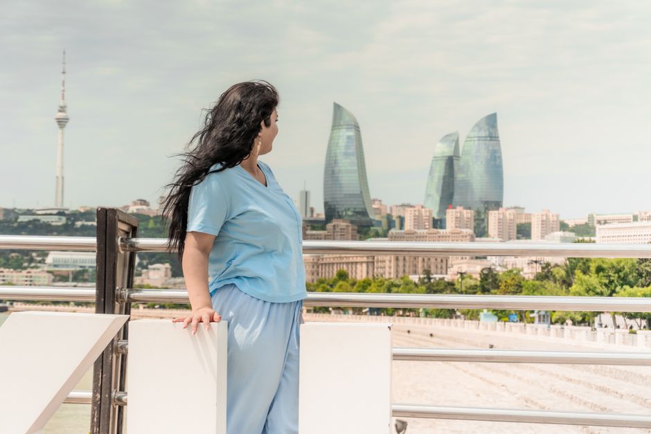 A woman stands on a balcony, observing the Flame Towers in Baku, Azerbaijan.