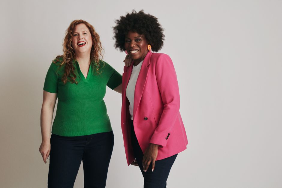 Two women smiling indoors, showcasing casual fashion with a white background in a studio setting.
