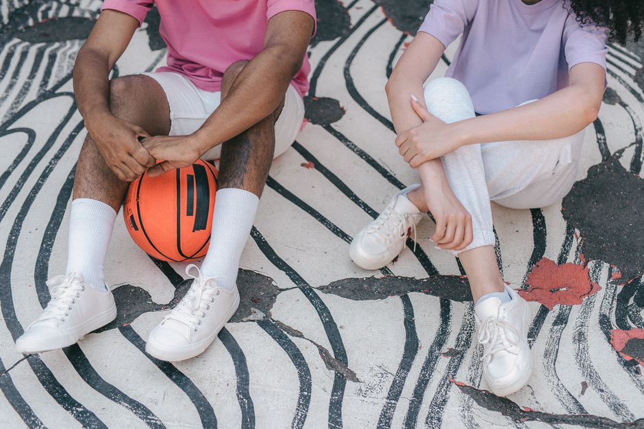 Two friends sitting on patterned pavement with a basketball, enjoying a casual outdoor moment.