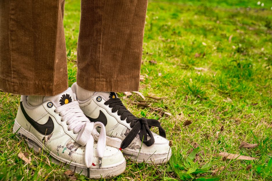 A close-up of trendy sneakers and corduroy pants standing on grass, showcasing urban style.