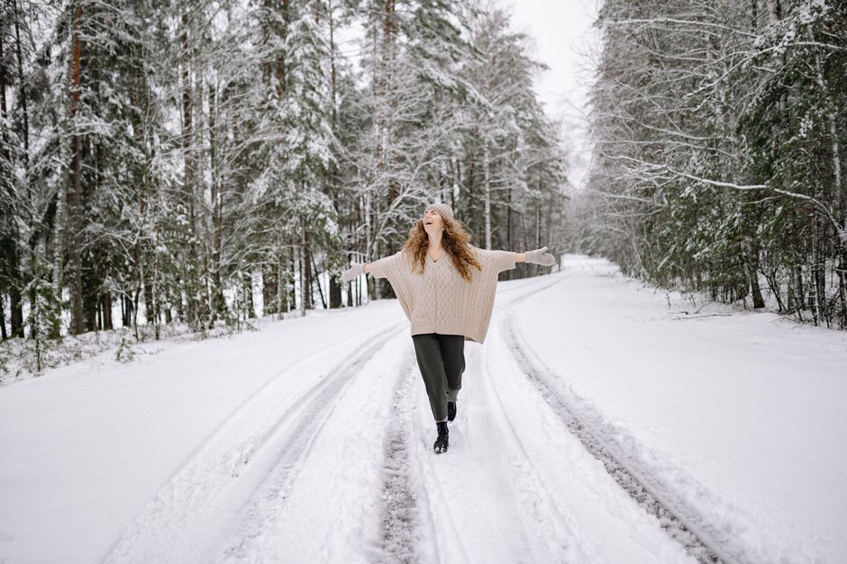 A cheerful woman with curly hair walks joyfully on a snow-covered forest road in winter.