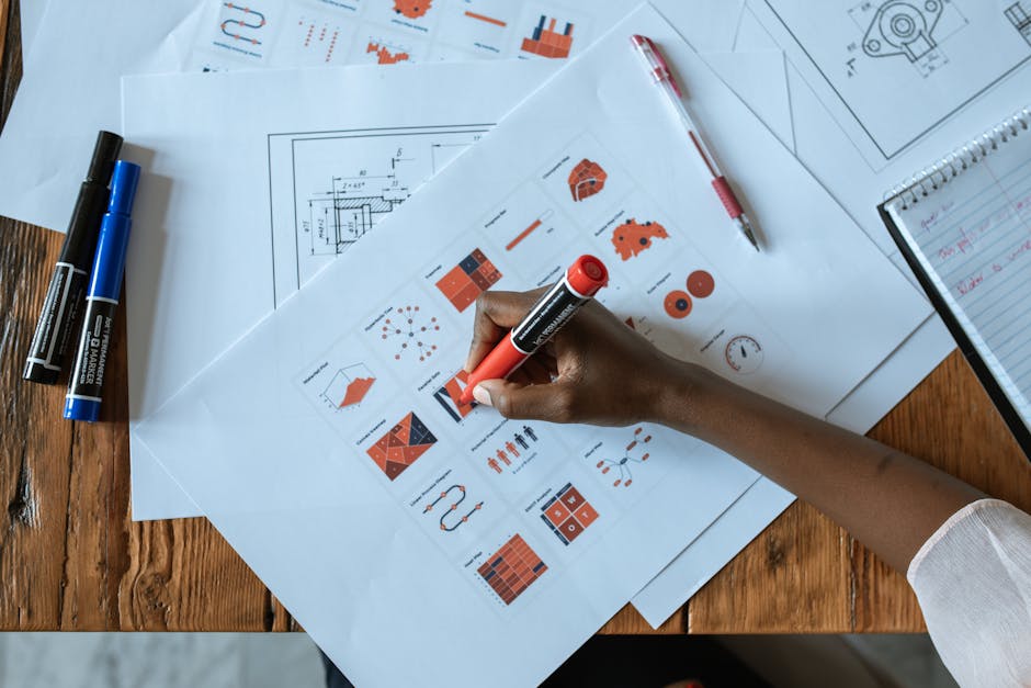 Overhead view of a person marking business charts with a red marker on a wooden table.